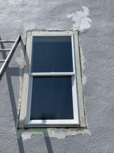 gray stucco wall with cracks with white window and trim partially removed