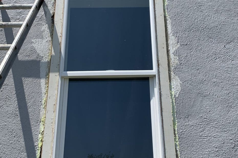 gray stucco wall with cracks with white window and trim partially removed