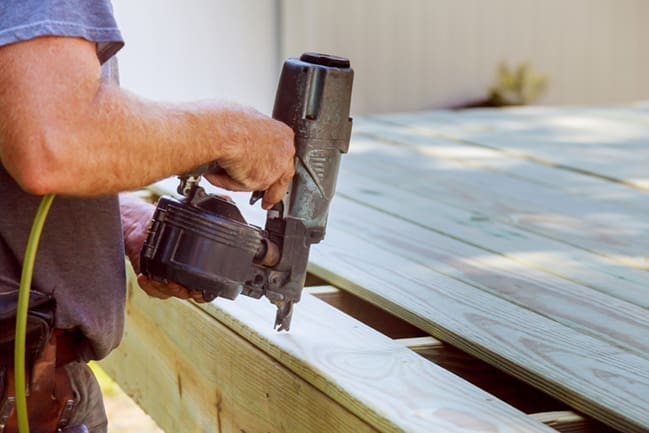 Contractor repairing an outdoor deck with a nail gun